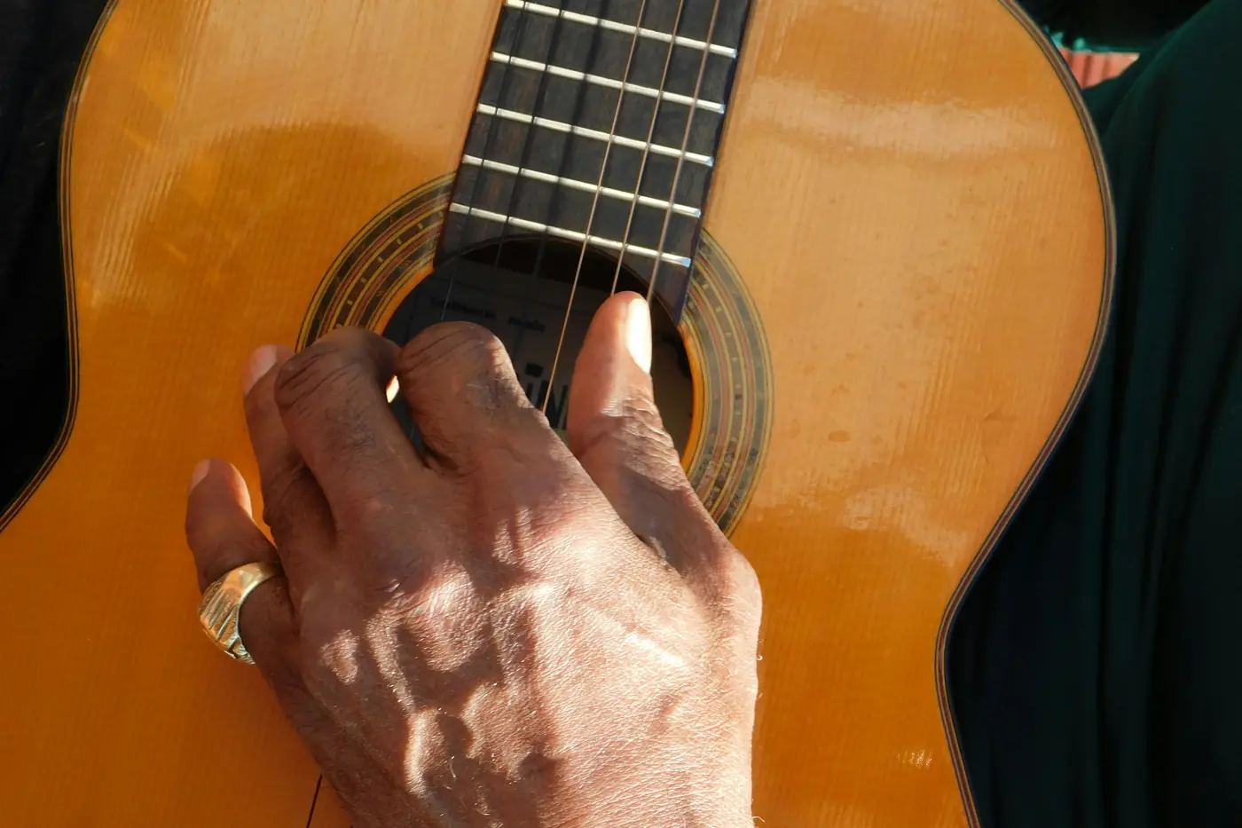 A close-up of a hand pressing the strings of an orange-brown flamenco guitar above the sound hole.