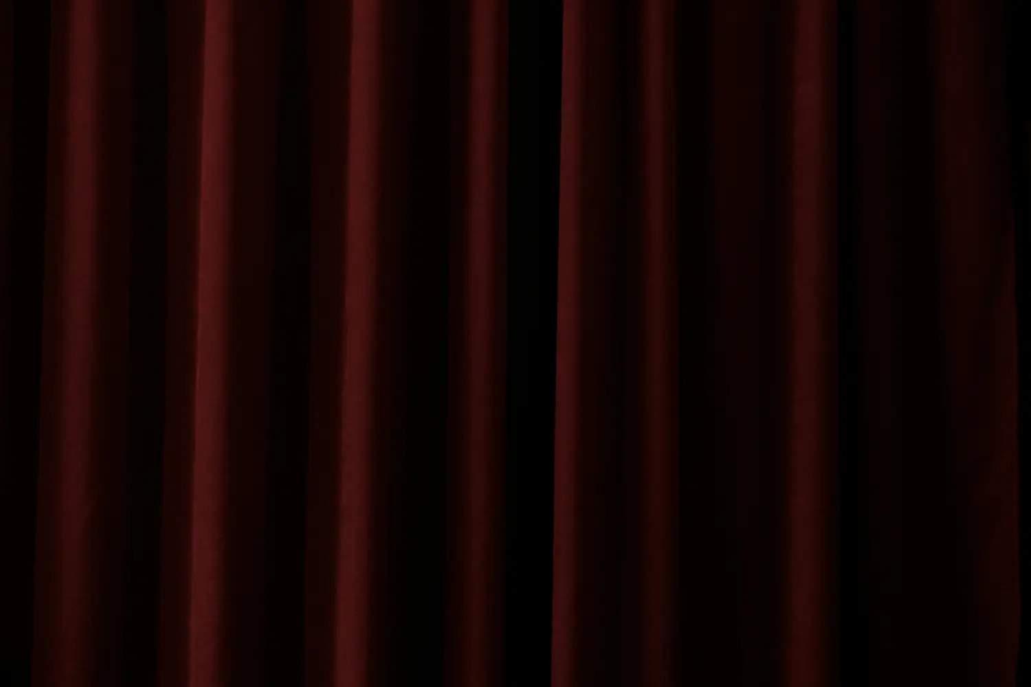 Dark red velvet theatre curtains hanging in deep vertical folds.